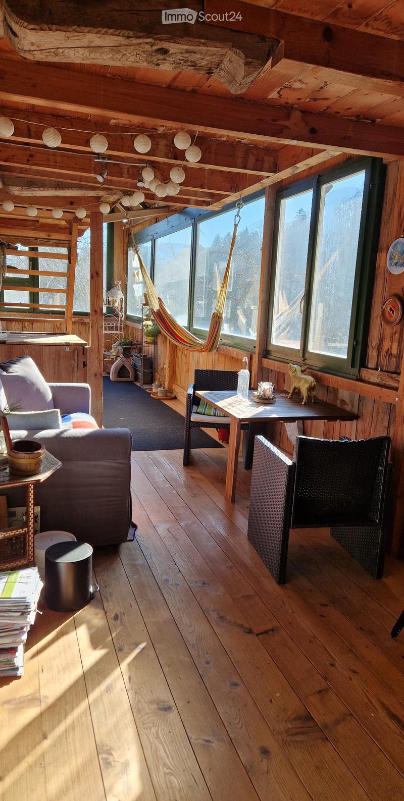 Cozy wooden room with large windows, a sofa, a small table, chairs, a hammock, and a pet bed.