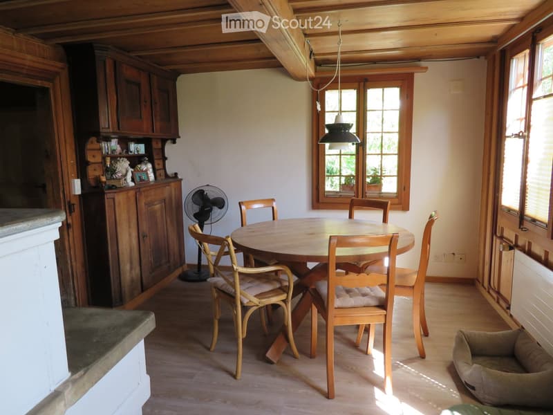 Cozy dining area with wooden table, chairs, and built-in wooden cabinetry. Features a hanging pendant light, a small fan, and a pet bed in the corner.