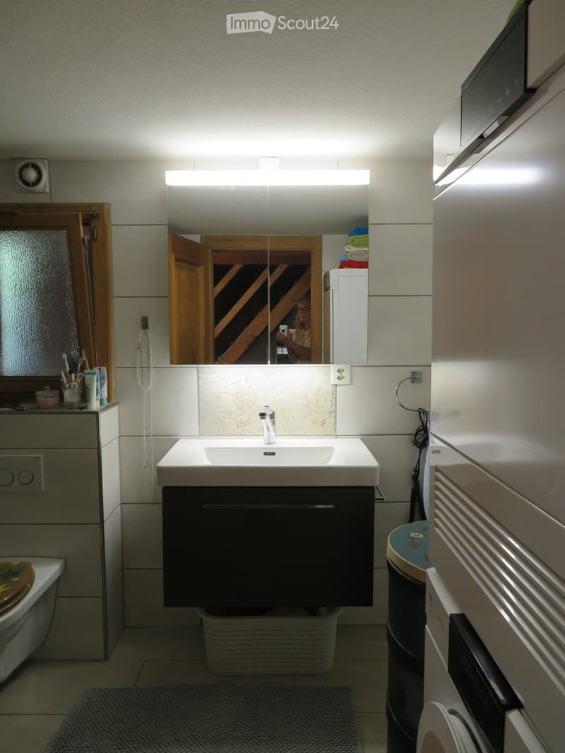 Modern bathroom with a white sink, mirror, and cabinet. Features a bathtub, toilet, and radiator. The mirror has built-in lighting.