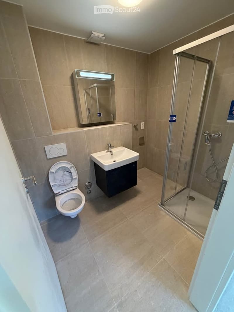 Modern bathroom with beige tiles, a toilet, a sink with a mirror, and a glass-enclosed shower.