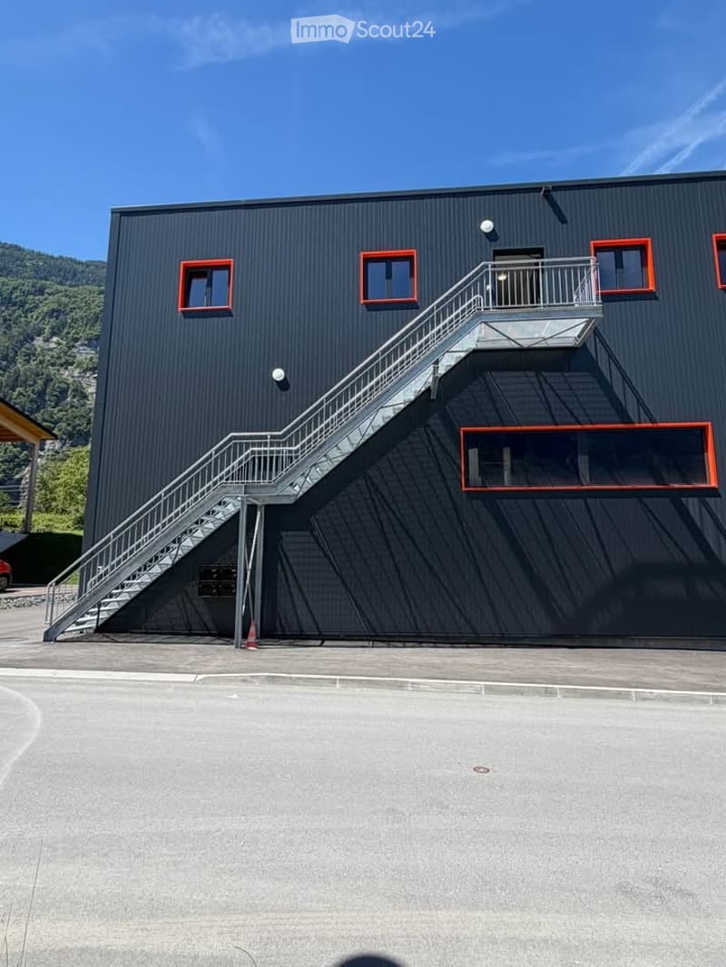 Modern black building with red-framed windows, external staircase leading to a balcony, and a clear view of surrounding greenery.