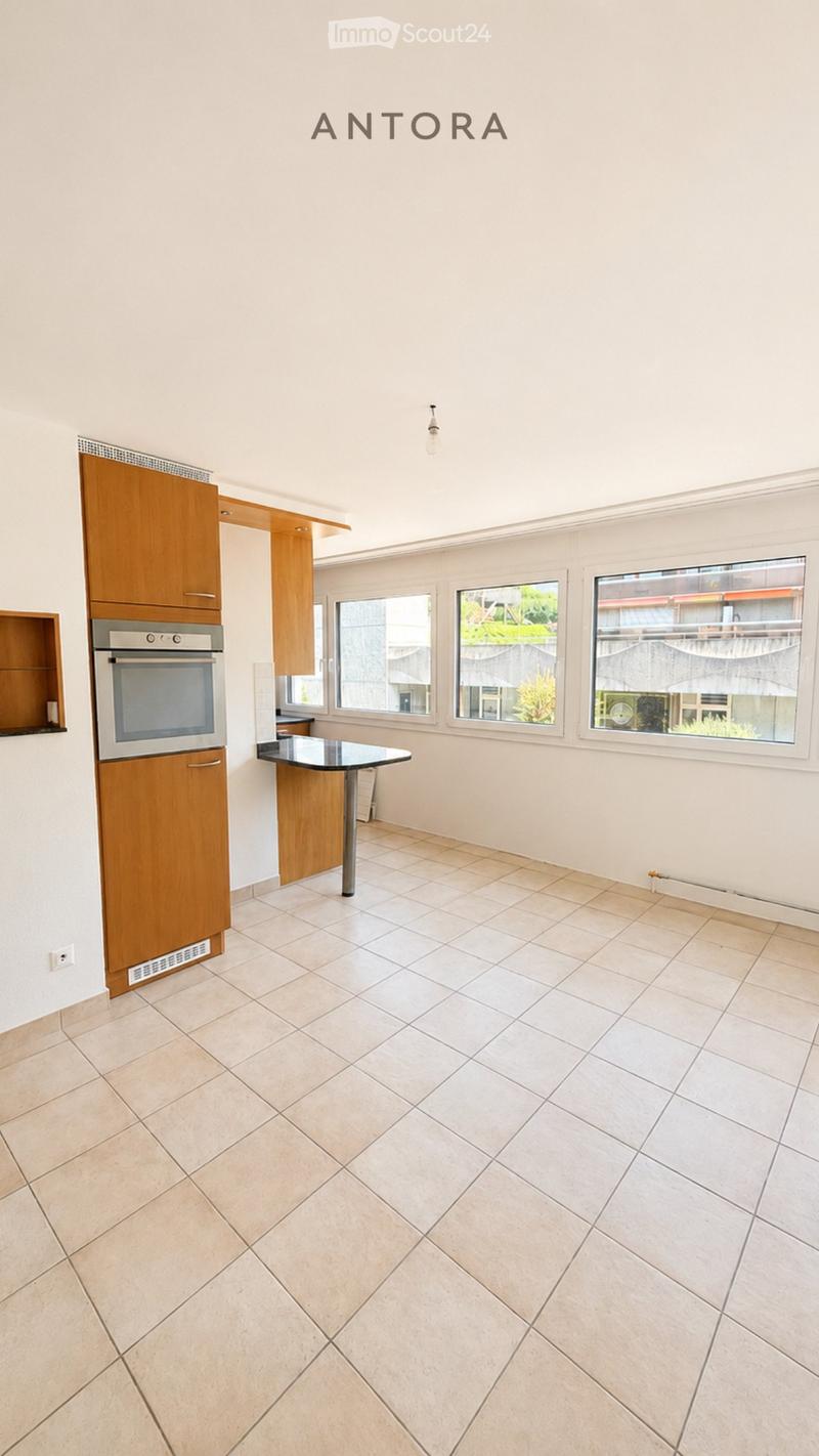 Modern kitchen with tiled floor, white walls, wooden cabinets, built-in oven, and a central table.