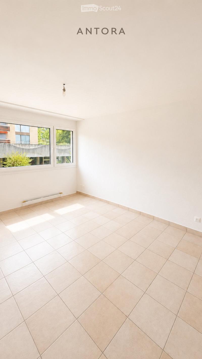 Empty room with light-colored tiled flooring and white walls, featuring two windows with a view of greenery outside.