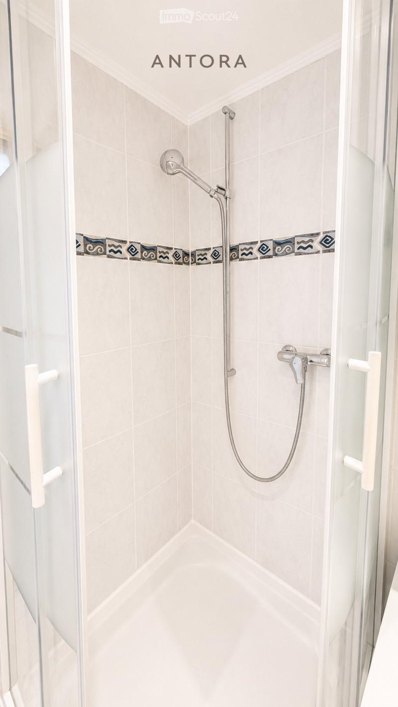 Modern shower area with white tiles, a decorative border, and a glass enclosure. Features a handheld showerhead and a built-in faucet.