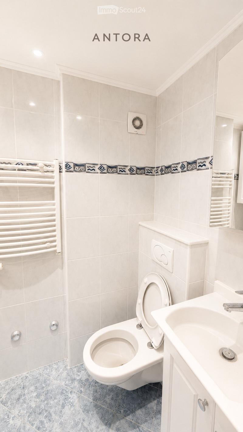 Modern bathroom with white tiles, a toilet, a sink, and a radiator. The walls feature a decorative border with blue and black patterns.