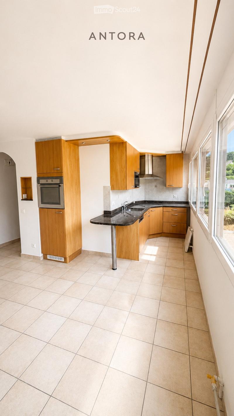 Modern kitchen with light wooden cabinets, stainless steel oven, black countertop, and tiled floor.