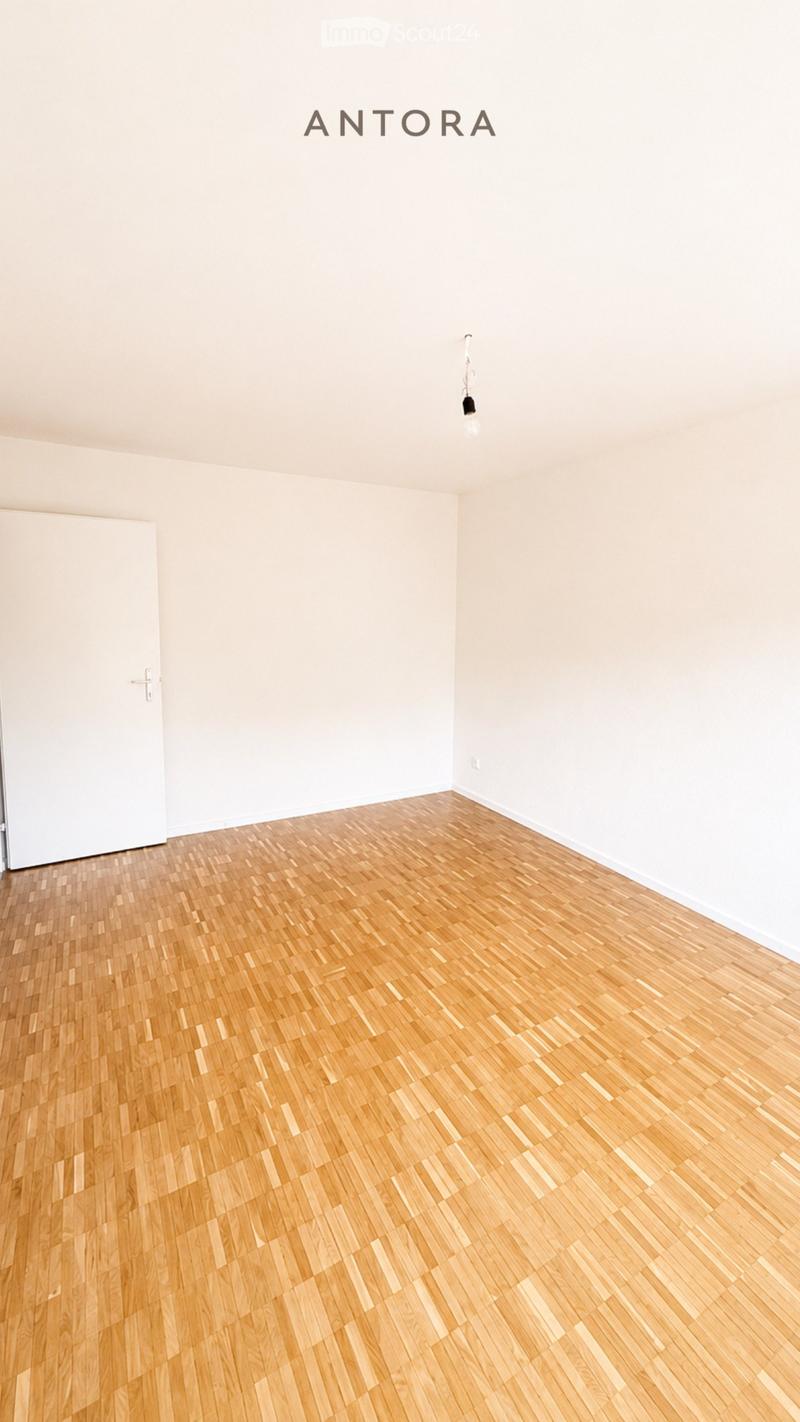 Empty room with light wooden flooring and white walls, featuring a single door and a light fixture on the ceiling.