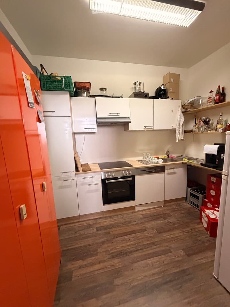 Modern kitchen with white cabinets, stainless steel appliances, wooden flooring, and various kitchen items on the counter.