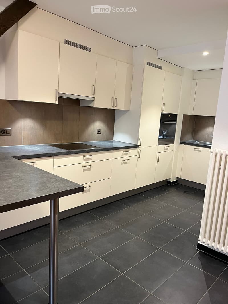 Modern kitchen with white cabinets, dark countertops, and black tiled flooring. Features a sink, oven, and stove.