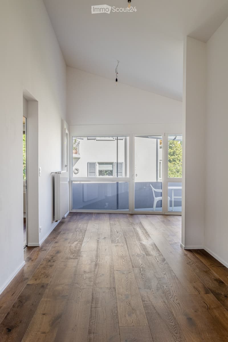 Bright, empty room with wooden flooring, white walls, and large sliding glass doors leading to a balcony area.