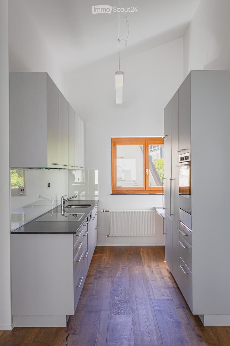 Modern kitchen with white cabinets, dark countertops, wooden flooring, and a large window with wooden frame.