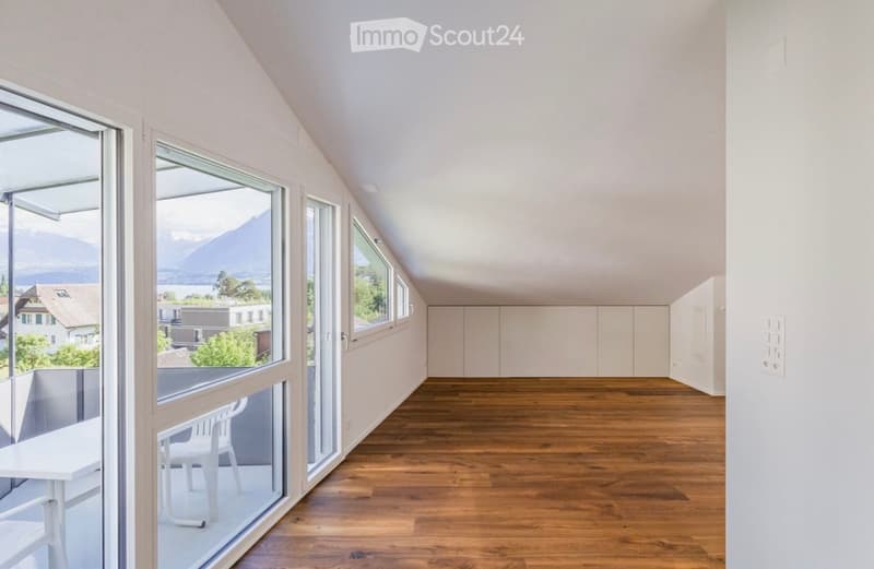 Bright, airy room with wooden flooring, large windows offering a scenic mountain view, and a small table with a chair near the window.