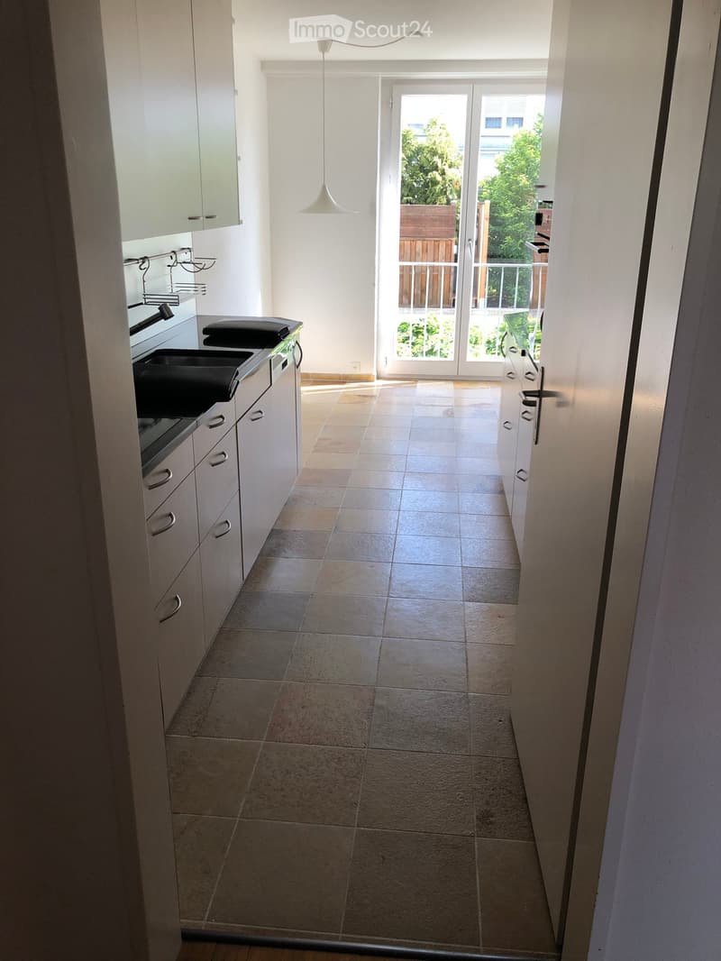 Modern kitchen with white cabinets, tiled floor, and a sliding glass door leading to a balcony.