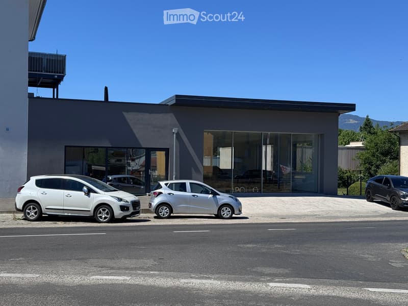 Modern building with large glass windows and a flat roof, with several cars parked in front.