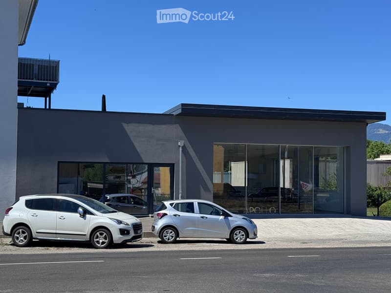 Modern building with large glass windows and a flat roof, with two parked cars in front.