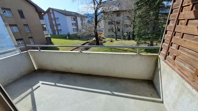 Outdoor balcony with a railing, concrete floor, and surrounding greenery