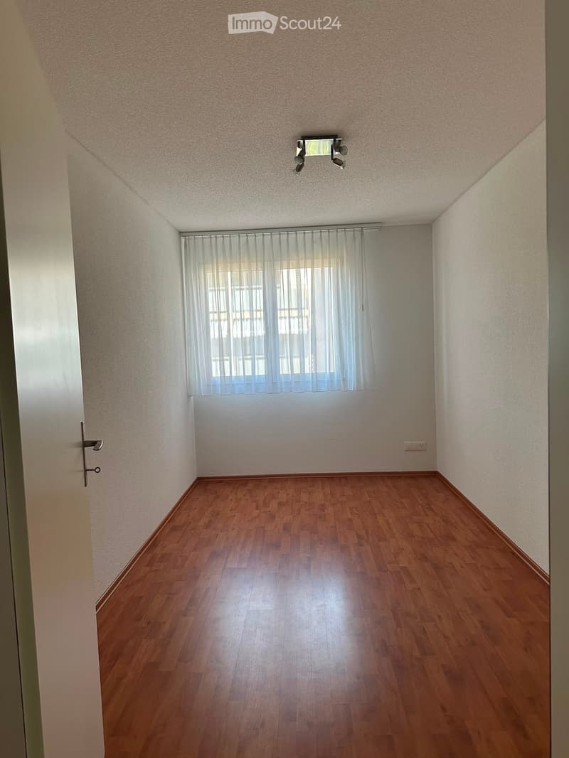 Empty room with wooden flooring, white walls, and a window with sheer curtains. No furniture or equipment is present.