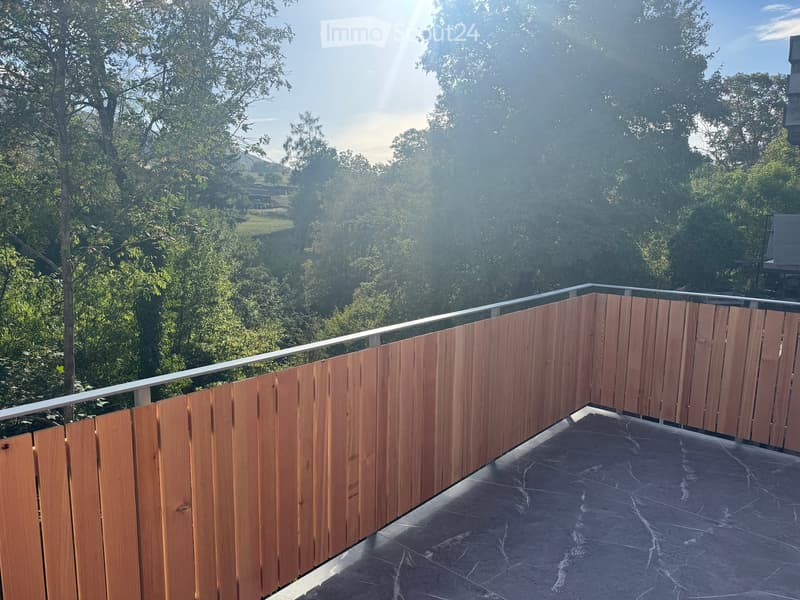 Balcony with wooden privacy screens, metal railing, and a view of a lush, green landscape.