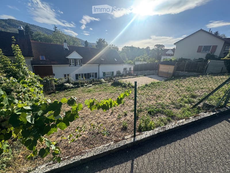 A fenced garden area with a gravel path, vines, and a view of a house and surrounding landscape.