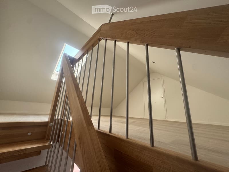 Modern wooden staircase with metal balustrade, leading to an open area with a skylight above.