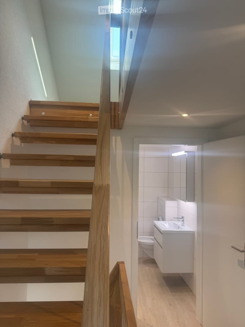 Wooden staircase leading to a modern bathroom with white tiles, a sink, and a toilet.