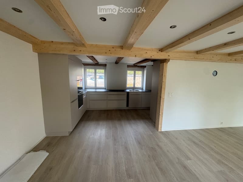 Modern kitchen with light grey cabinets, wooden flooring, and exposed wooden beams on the ceiling. Features a sink, faucet, and oven.