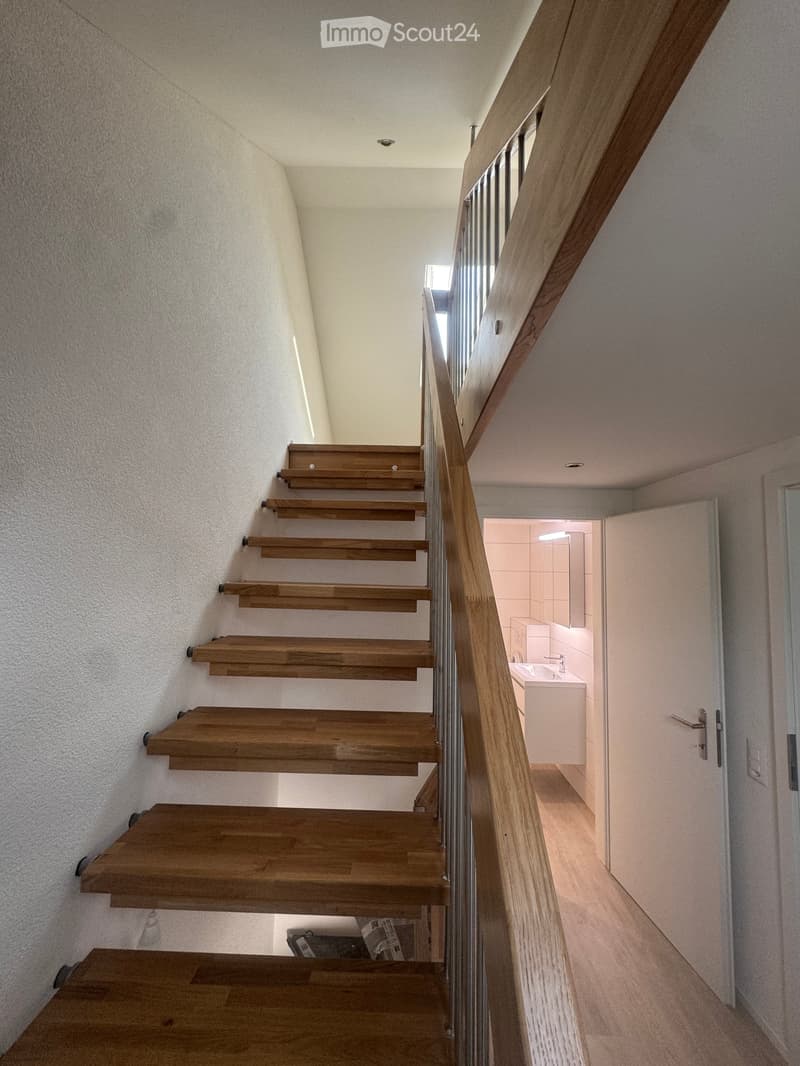 Modern staircase with wooden steps and a glass railing, leading to a small bathroom with white tiles and a sink.