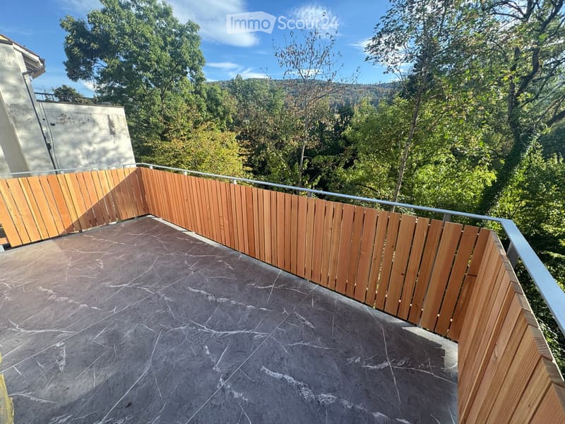 Wooden fence and metal railing on a rooftop terrace with a view of trees and hills.
