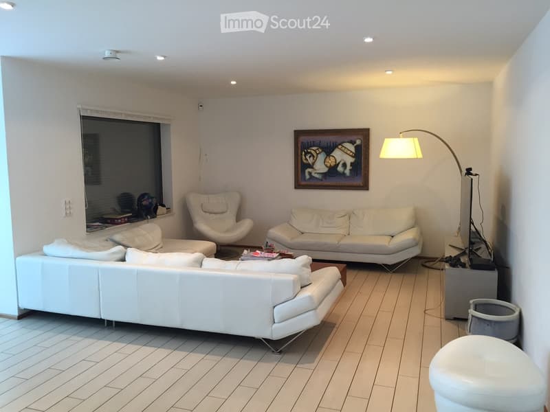 Modern living room with white leather sofas, a white armchair, a floor lamp, a coffee table, and a picture frame on the wall.