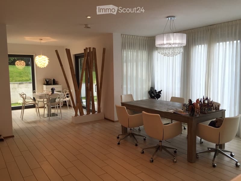 Open-plan dining and office area with modern furniture, large windows with curtains, and decorative wooden sculptures.
