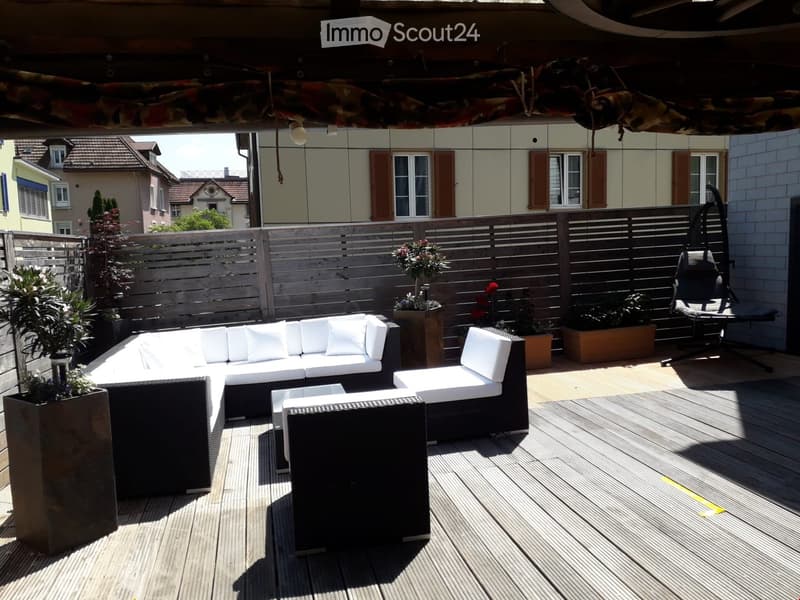 Wooden deck with white outdoor sofa, matching chairs, small table, and potted plants.