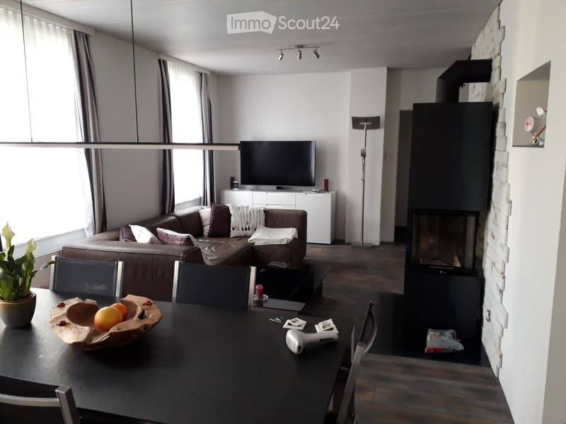 Modern living room with a sectional sofa, coffee table, dining table with chairs, television, floor lamp, fireplace, and decorative bowl with fruit.