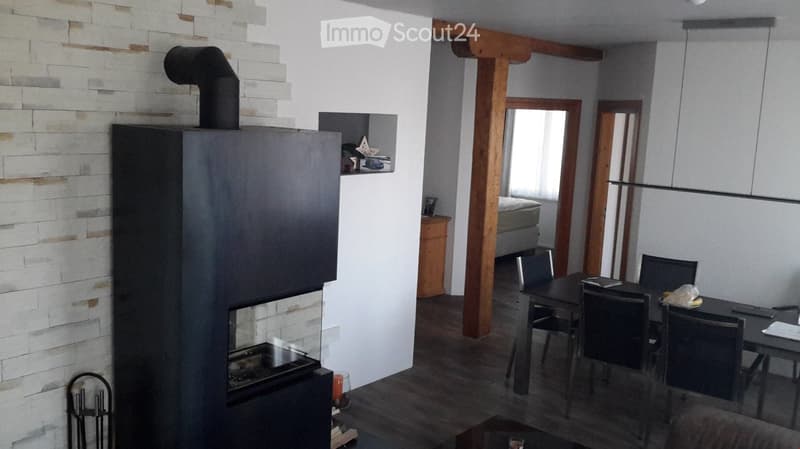 Modern living and dining area with a large fireplace, dining table with chairs, and a sofa in the background.