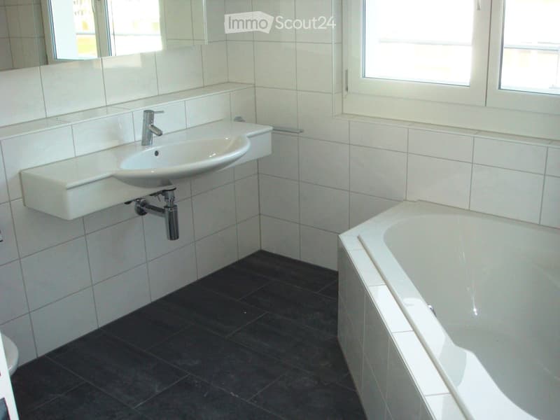Modern bathroom with white tiled walls, dark tiled floor, white sink with chrome faucet, and bathtub.