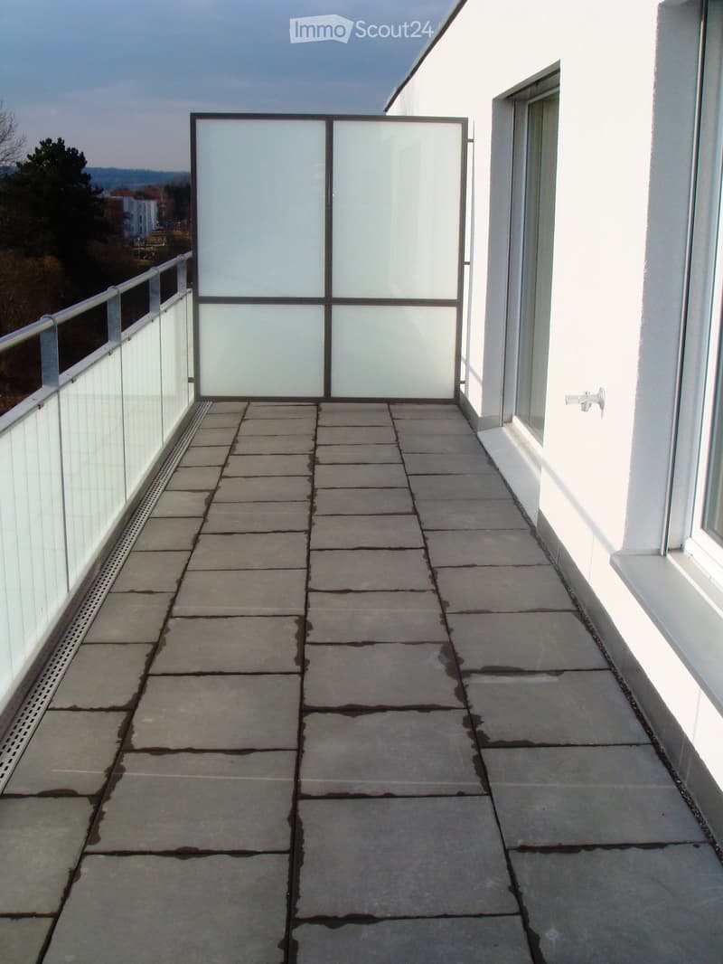 Modern balcony with white tiled floor, grey tiled wall, and glass panels, featuring a small decorative item in the center.