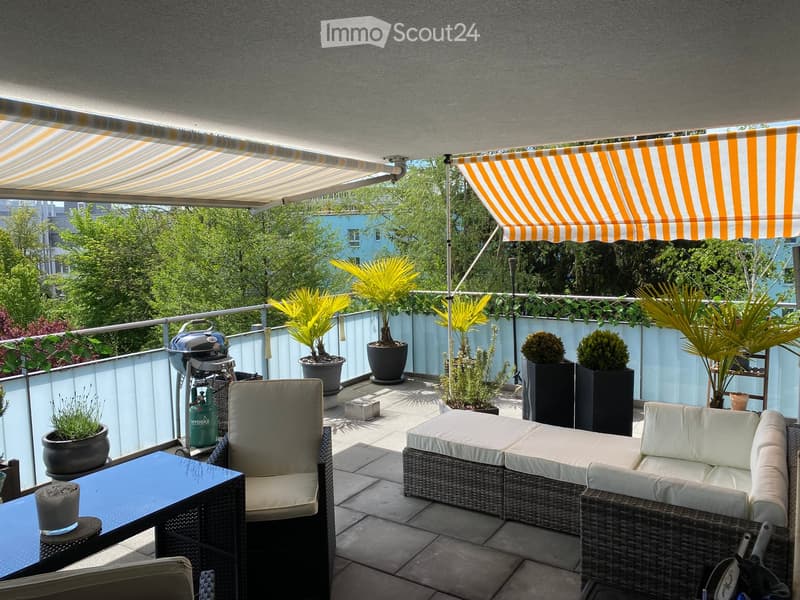 Balcony with wicker furniture, sofa, table, chairs, grill, potted plants, and striped awnings.