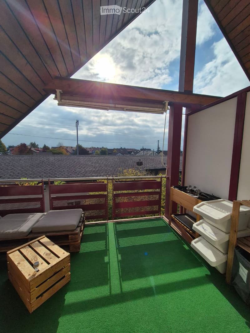 Balcony with green artificial turf, wooden pallets used as seating and table, red privacy screens, and a small sink area.