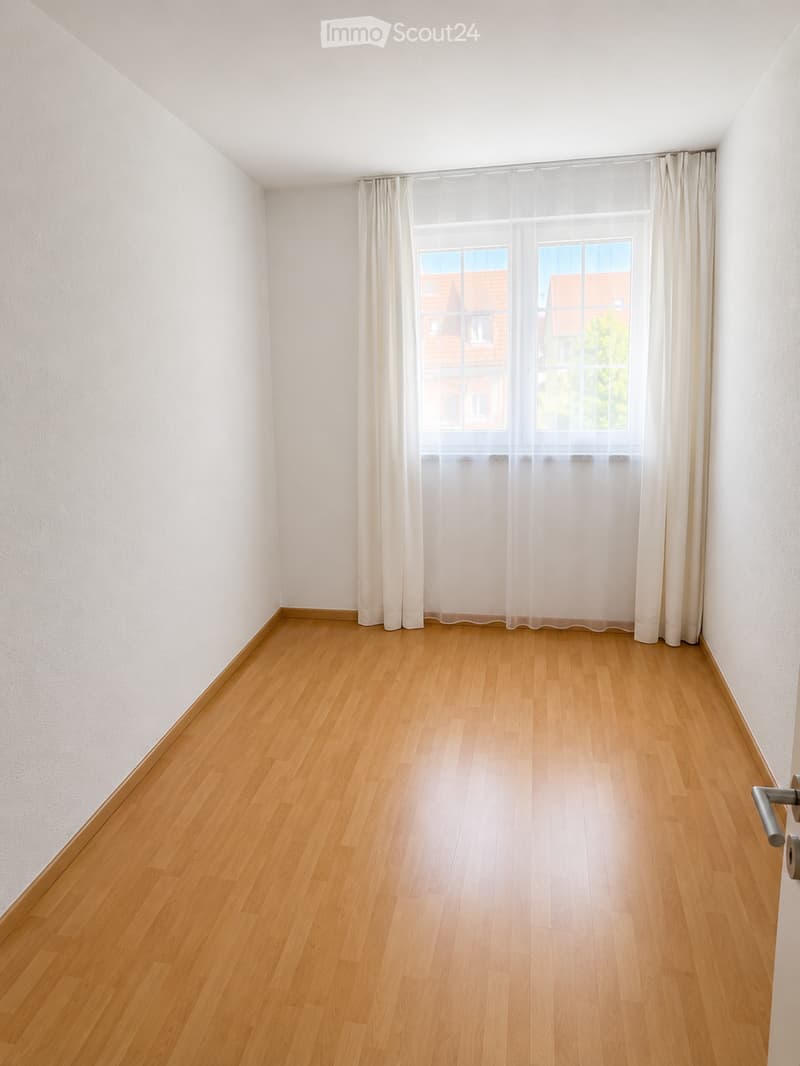 Empty room with wooden flooring, white walls, and large windows with sheer curtains. No furniture or equipment present.