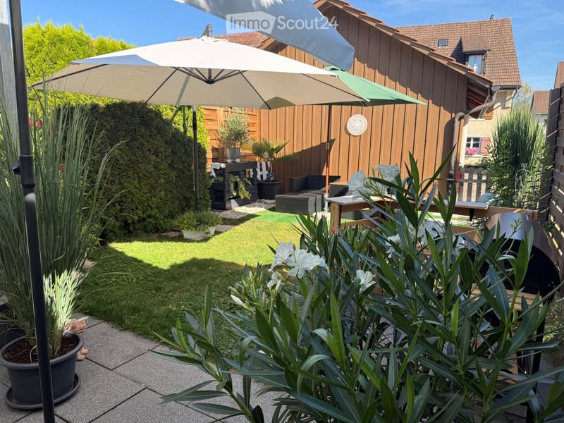Well-maintained garden with a patio, outdoor furniture, potted plants, and a small lawn area.