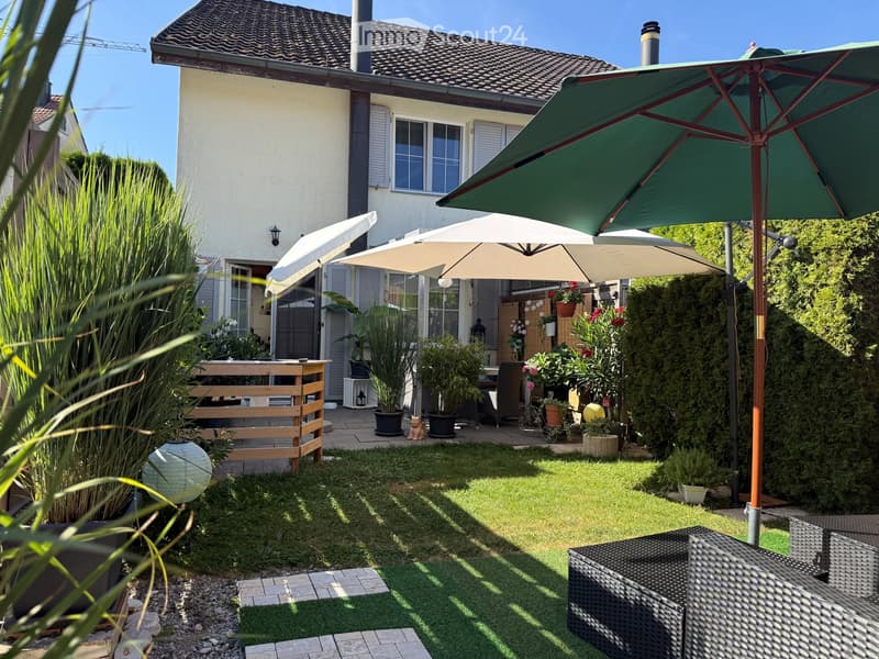 Well-maintained garden with artificial grass, patio furniture, large umbrellas, potted plants, and a wooden deck area.