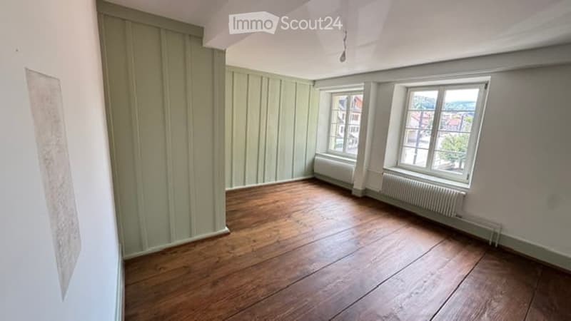 Empty room with wooden flooring, white walls, and two windows with radiators underneath. No furniture or equipment present.