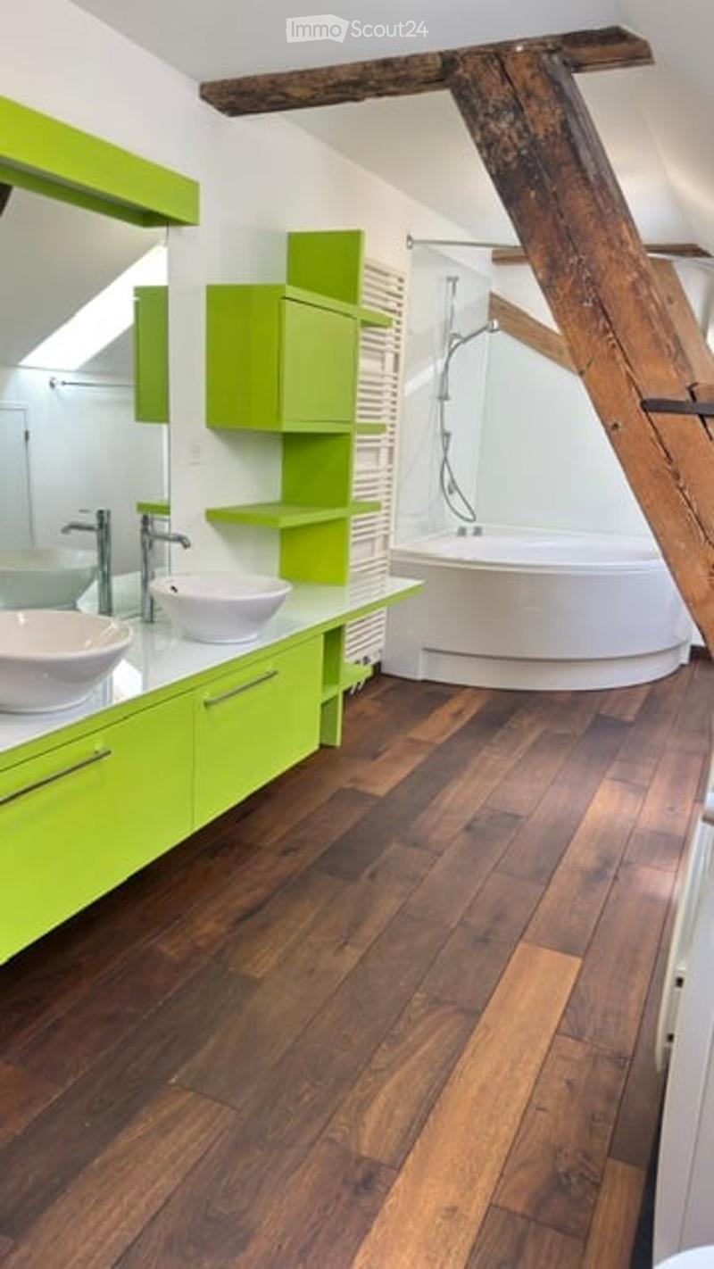 Modern bathroom with green cabinets, white sinks, a bathtub, and wooden flooring.