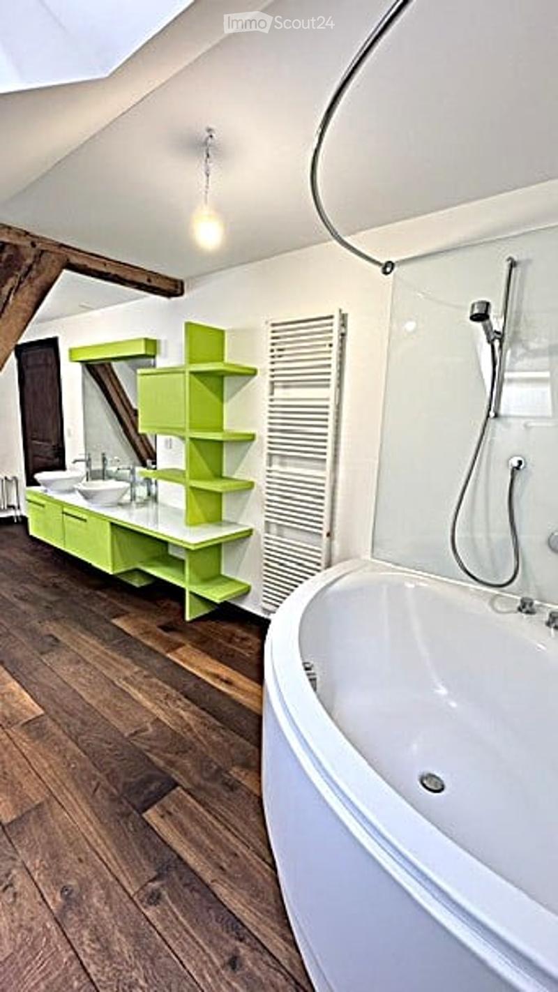 Modern bathroom with a freestanding bathtub, double sink vanity with green shelving, wooden flooring, and exposed wooden beams on the ceiling.
