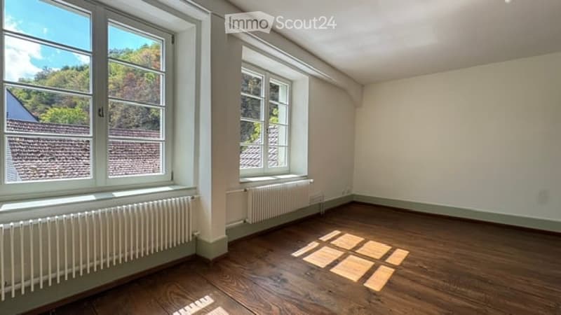 Empty room with wooden flooring, large windows, radiators, and natural light. No furniture or equipment present.