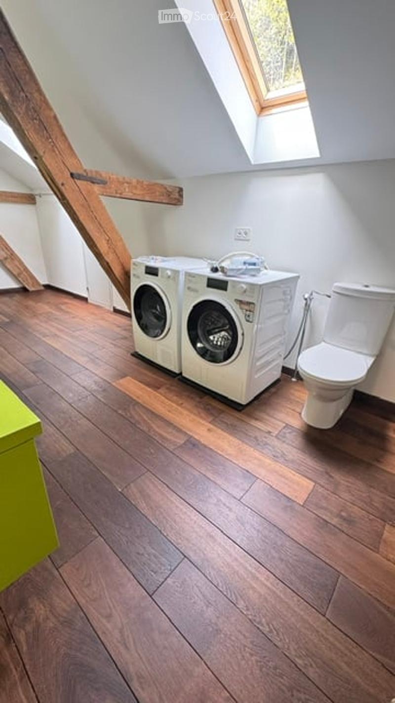 Bright, modern bathroom with wooden flooring, white walls, and a skylight. Features a washing machine and a toilet.