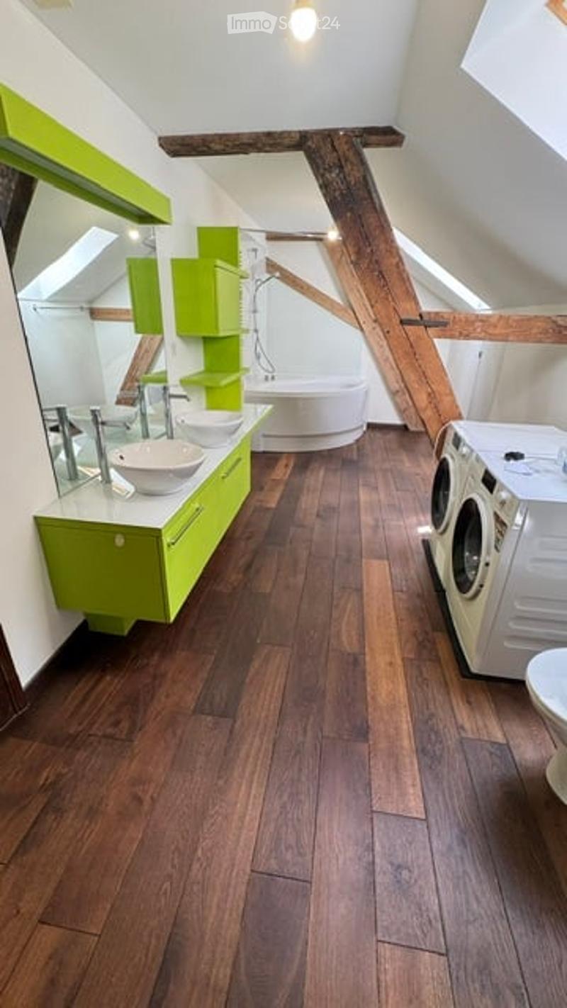 Modern bathroom with wooden flooring, green cabinets, a large mirror, a bathtub, and a washing machine.