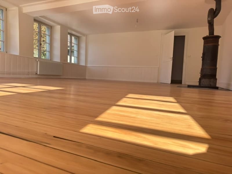 Empty room with wooden flooring, white walls, large windows, radiator, and a closed door.