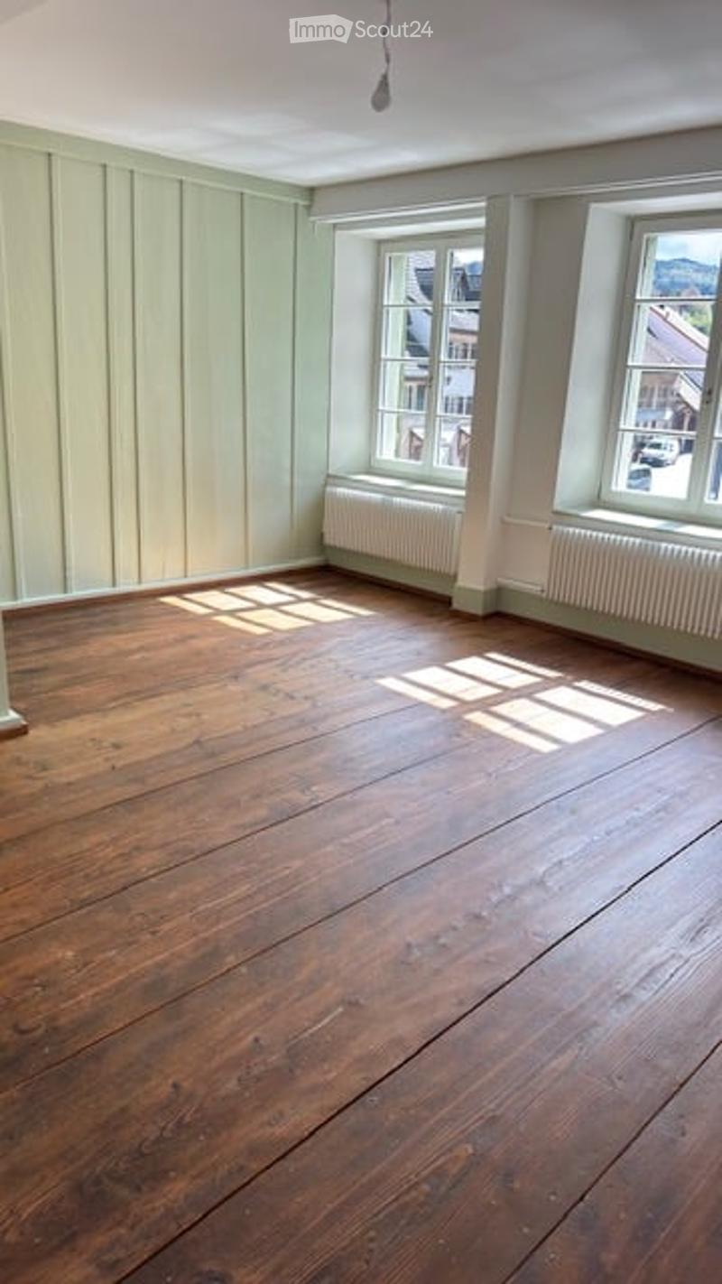 Completely empty room with wooden flooring, white walls, and two windows with radiators underneath.