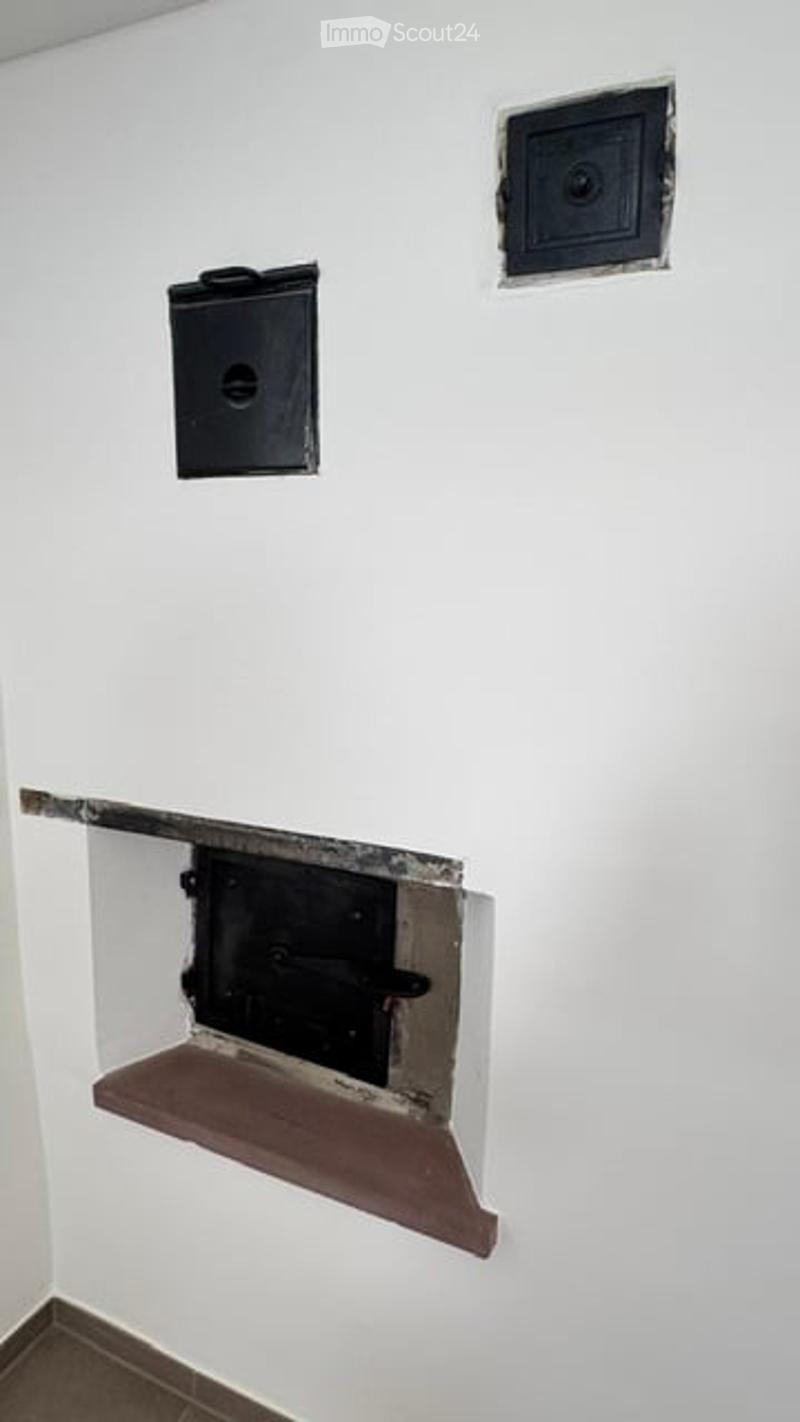 Empty room with a fireplace opening and two black vents on the wall.