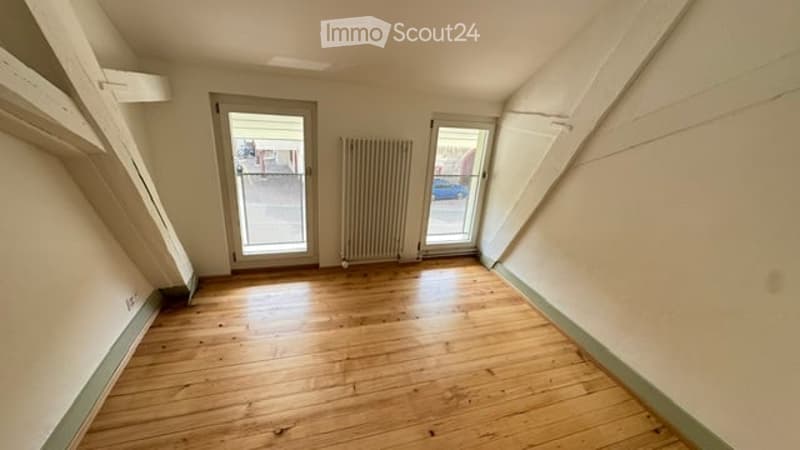Empty room with wooden flooring, two doors, and a radiator. No furniture or equipment present.